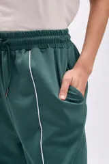 Pantalón deportivo ancho de color verde oscuro, con vivo blanco vertical en el centro de cada pierna. Presenta cordón de ajuste en la cintura y corte holgado.