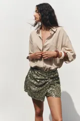 Falda pantalón verde militar con lentejuelas plateadas y negras, de tiro alto, con delantero cruzado y nudo.
