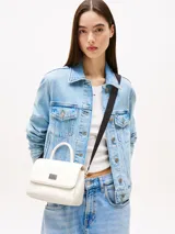 Cartera Tommy Jeans color blanco, con asa superior y correa de hombro ajustable en color negro. Tiene cierre de solapa magnético, dos compartimentos principales y un bolsillo interior con cremallera.