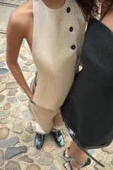 Top chaleco color beige de cuello halter con espalda descubierta y trabilla con hebilla metálica. Cierre frontal con botones y ganchos metálicos.