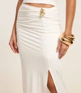 Conjunto de dos piezas color blanco, compuesto por un top tipo corset strapless con escote en V y una pollera midi ajustada con fruncido lateral y abertura alta, asegurada con un adorno metálico.