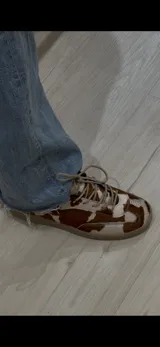 Zapatillas bajas de cuero con estampado de vaca en blanco y marrón.