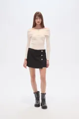 Short de jean color beige claro, tiro alto, corte ajustado y diseño cruzado con botones dorados decorativos en el lateral.