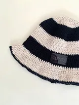 Sombrero tipo bucket tejido a crochet a mano, con hilo 100% algodón y diseño a rayas en tonos rosa y rojo. Presenta una etiqueta con el logo de la marca Cilento en el frente.