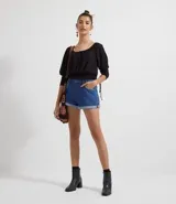 Blusa de poliéster negra con mangas largas abullonadas, escote redondo con botones y bordado en el frente. Tiene volados en el ruedo y ajuste con lazos en los laterales.