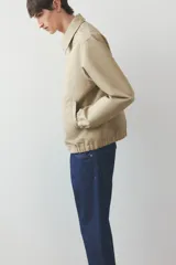 Campera color beige de denim rígido con cuello clásico, cierre frontal, bolsillos insertados al bies y un bolsillo interior. Elástico revestido en puños y bajo. Corte estándar y forrada.
