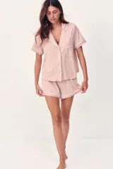 Pijama corto de dos piezas color rosado, en tejido de punto suave con ribetes blancos en contraste. Incluye camisa de manga corta con cuello abierto, botones al frente y bolsillo superior, y short con cintura elástica.