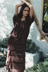 Vestido midi color marrón oscuro confeccionado en hilatura con viscosa y algodón. Tiene cuello redondo, manga corta y bajo con volantes desflecados y aberturas laterales.