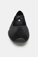 Zapato plano deportivo tipo bailarina, color negro, con cuerpo de material textil y tiras elásticas cruzadas en el empeine. Presenta punta redonda y suela engomada.