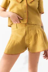Short color ocre de lino con pinzas, cintura alta y detalles bordados a contratono en ruedo y bolsillos.