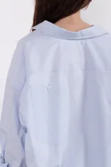 Camisa celeste con botones en el frente, cuello camisero, bolsillo en la espalda y fit amplio.