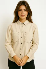 Camisa de jean negra con cuello clásico, cierre frontal con botones a presión, dos bolsillos con solapa en el pecho y tachas plateadas decorativas en cuello, hombros y bolsillos.