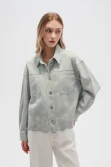 Campera de jean color crudo, de corte recto, con cuello clásico, cierre frontal con botones metálicos, dos bolsillos con solapa en el pecho y bajo con detalle de bordado calado.