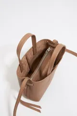 Bolso de mano Bimba y Lola modelo Chihuahua, tamaño mini, color marrón topo, fabricado en piel con piezas de metal plateado. Presenta estructura blanda, cierre con cinta de piel, logo metálico, bolsillo interior con cremallera e interior con logo grabado.