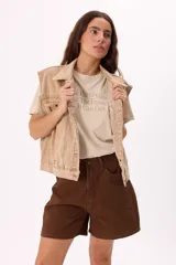 Chaleco de denim color beige con lavado desgastado, corte relajado y bolsillos frontales.