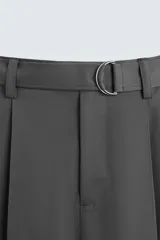 Pantalón negro de corte amplio con cinturón de tela con hebilla metálica. Presenta pliegues frontales, bolsillos laterales y traseros. Cierre frontal con cremallera y botón.