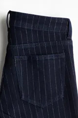 Jeans de cinco bolsillos en denim azul marino con leve stretch. Diseño de raya diplomática con hilos brillantes en la trama. Corte ajustado de cintura a cadera y acampanado desde la rodilla al bajo. Modelo de tiro bajo con cierre y botón.