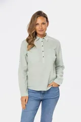 Camisa color beige de lino, de manga larga con botones metálicos personalizados y presilla en la manga. Tiene cuello clásico, cierre frontal parcial con botones y bolsillo de parche en el pecho.