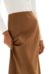 Pollera midi color marrón con leve brillo y caída suave. Modelo de tiro alto con elástico oculto en la cintura y leve vuelo en el bajo.