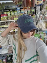 Gorro tipo jockey de tela denim azul gastado, con visera curva y bordado frontal en hilo verde que dice "COSTA DULCE".