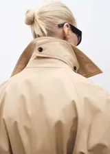 Abrigo color beige con cuello solapa, doble botonadura, cinturón y bolsillos laterales.