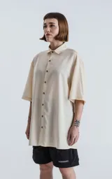 Camisa oversize color crema con cuello clásico, cierre frontal con botones marrones y mangas cortas.