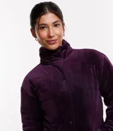 Campera deportiva de terciopelo color violeta, con cuello alto, cierre de botones, bolsillos laterales y puños ajustados.