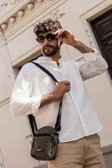 Morral bandolera negro de poliéster con correa ajustable y múltiples bolsillos con cierre.