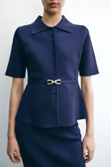 Chaqueta azul marino de punto con cuello solapa y manga corta. Incluye cinturón fino con hebilla dorada y cierre frontal con botones a tono.