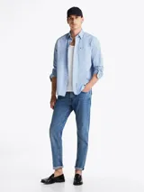 Camisa celeste de corte amplio confeccionada en sarga de puro algodón teñido en prenda, con cuello abotonado, bolsillo de parche en el pecho, puños redondeados con botón y logo de Tommy Hilfiger bordado en el bolsillo del pecho.