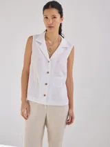 Camisa blanca sin mangas, con cuello camisero, cierre frontal con botones de madera y bolsillo de parche en el pecho.