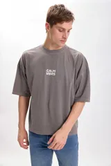 Remera gris con estampa en la espalda que dice "Calm Vibes" con una flor en el medio. Corte amplio y recto, con proporciones cuadradas.