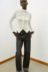 Jeans de tiro alto color negro lavado, con cintura cruzada, cinco bolsillos y pernera recta. El bajo está acabado en vuelta y tiene cierre frontal cruzado con cremallera y botones.