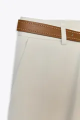 Pantalón negro de tiro alto con pernera recta, bolsillos frontales y falsos bolsillos con solapa en la espalda. Incluye cinturón marrón de cuero sintético.