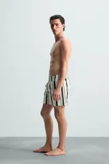 Bañador de hombre confeccionado en tejido técnico, color blanco con rayas verticales negras y celestes. Cuenta con cintura elástica ajustable con cordón, bolsillos laterales, bolsillo trasero y forro interior.