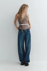Jeans de tiro medio color azul denim, corte baggy, con trabillas y cinco bolsillos. Cierre frontal asimétrico con cremallera y botones metálicos.