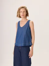 Top sin mangas de tela denim azul, con escote en V pronunciado y corte holgado. Presenta un pequeño ruedo con pespunte en el bajo.