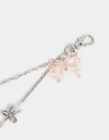 Llavero metálico plateado con cadenas y dijes de moños, mariposas de metal, corazones traslúcidos y flor rosa.