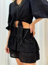 Minifalda negra con bordado inglés, cintura alta y detalle de argollas metálicas en el lateral.