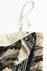 Vestido corto strapless con estampado de palmeras y flamencos. Presenta un frente cruzado con pliegues y un reborde de silicona en el escote. Incluye breteles finos ajustables opcionales y cierre lateral oculto.