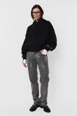Buzo negro tipo hoodie de frisa gamuzada, con silueta oversize, bolsillo canguro, puños y cintura de ribb a tono, capucha forrada en jersey y aplique de ojalillos metálicos en los puños.