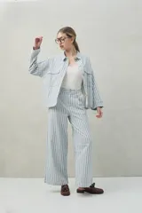 Pantalón de lino a rayas verticales azules y blancas, de corte amplio y relajado, con bolsillos laterales y cierre frontal con botón.