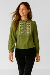 Blusa verde oliva de viscosa con bordado floral en el pecho, cuello mao con volados y mangas largas abullonadas. Cierre frontal con botones. Corte holgado.