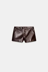 Shorts de tiro bajo color marrón oscuro con efecto piel brillante, cierre frontal con cremallera y gancho metálico, y bolsillos delanteros.