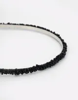 Vincha rígida de metal forrada en tela negra con aplique de mostacillas negras.