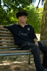 Chomba negra de corte cuadrado con cuello polo y mangas cortas. Presenta un escudo estampado en el pecho con diseño de fútbol retro y la palabra 'boxed' estampada en el frente.