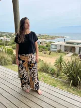 Pantalón palazzo de tiro alto, corte ancho (wide leg), con estampado botánico de hojas de palma en tonos negro, mostaza y beige.