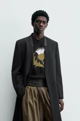 Levita negra de corte relajado confeccionada en tejido con lana. Presenta cuello sin solapa, mangas largas con puños abotonados, bolsillo de vivo en el pecho y bolsillos con solapa en la cadera. Incluye bolsillos interiores, abertura en el centro de la espalda y cierre frontal con botonadura.