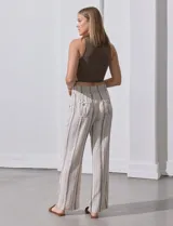 Pantalón de lino color beige con rayas verticales marrones, pretina ancha con punto smock y lazo ajustable, bolsillos verticales delanteros y bolsillos aplicados traseros.