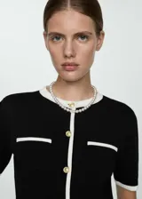 Cardigan de punto fino negro con ribetes blancos en cuello, cierre, bolsillos y mangas cortas.